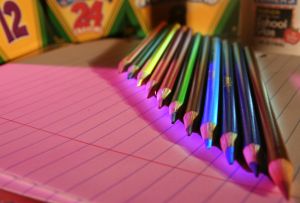 photo of colored pencils and crayon boxes on top of lined paper